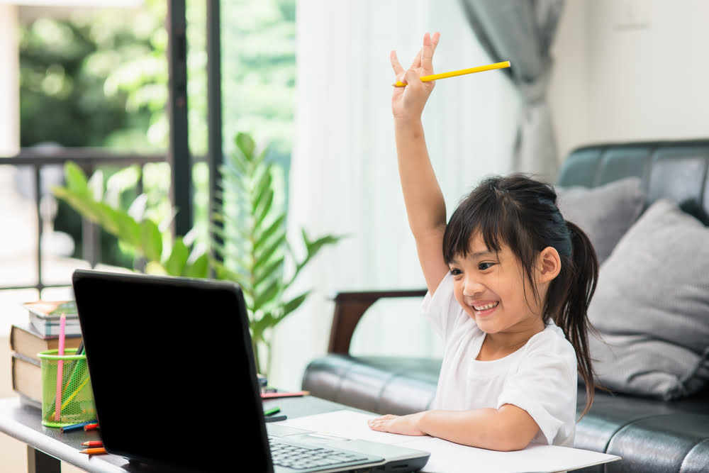 little girl with hand raised looking at a laptop